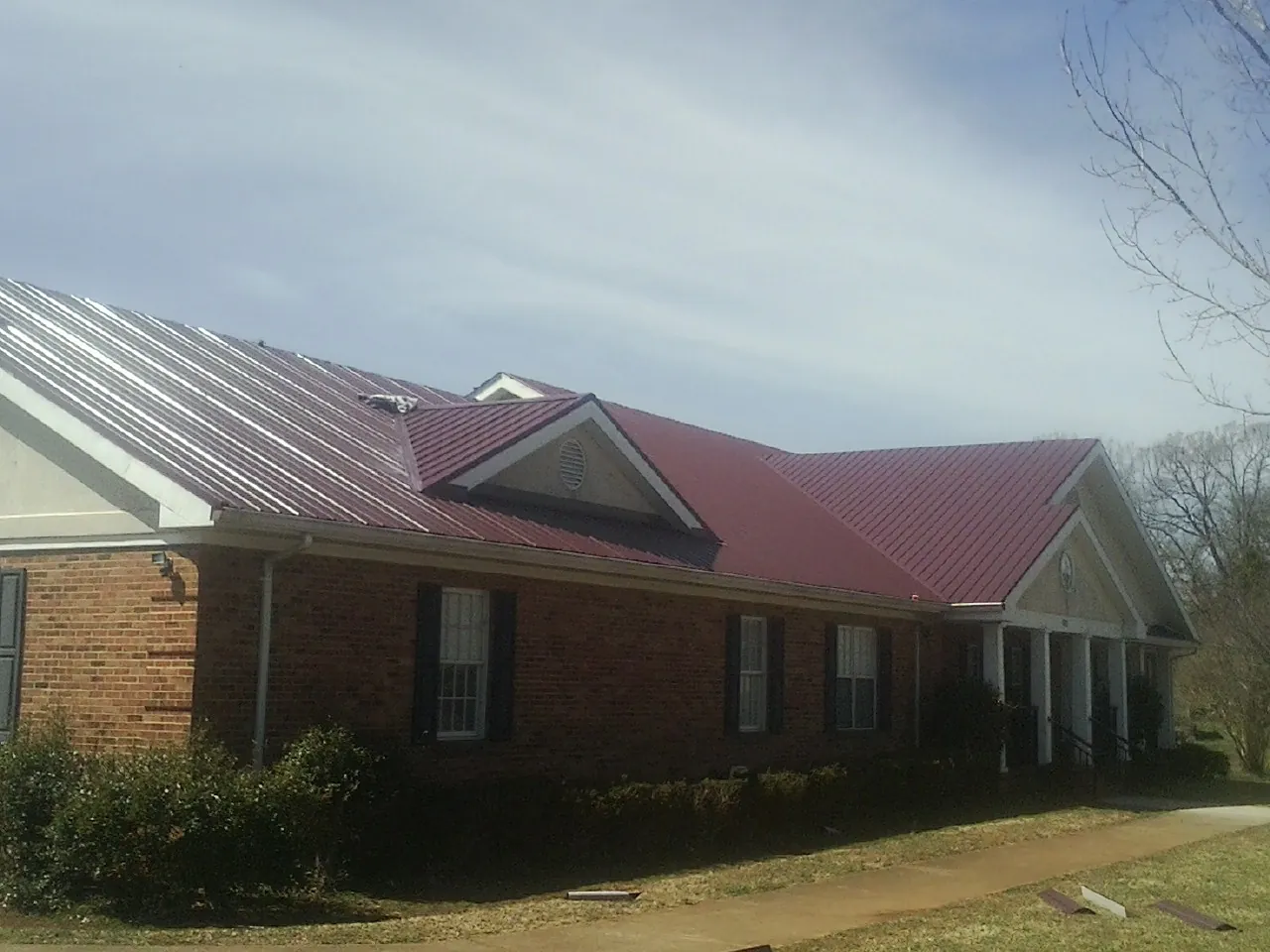 Red metal roof with gabled entries on a long brick building, from a Hail Damage Roof Repair job in Rushville