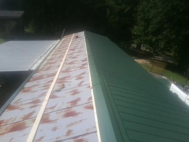 Old rusted panels beside newly installed green metal roofing — Wind Damage Roof Repair by Roofing Brothers in Rushville