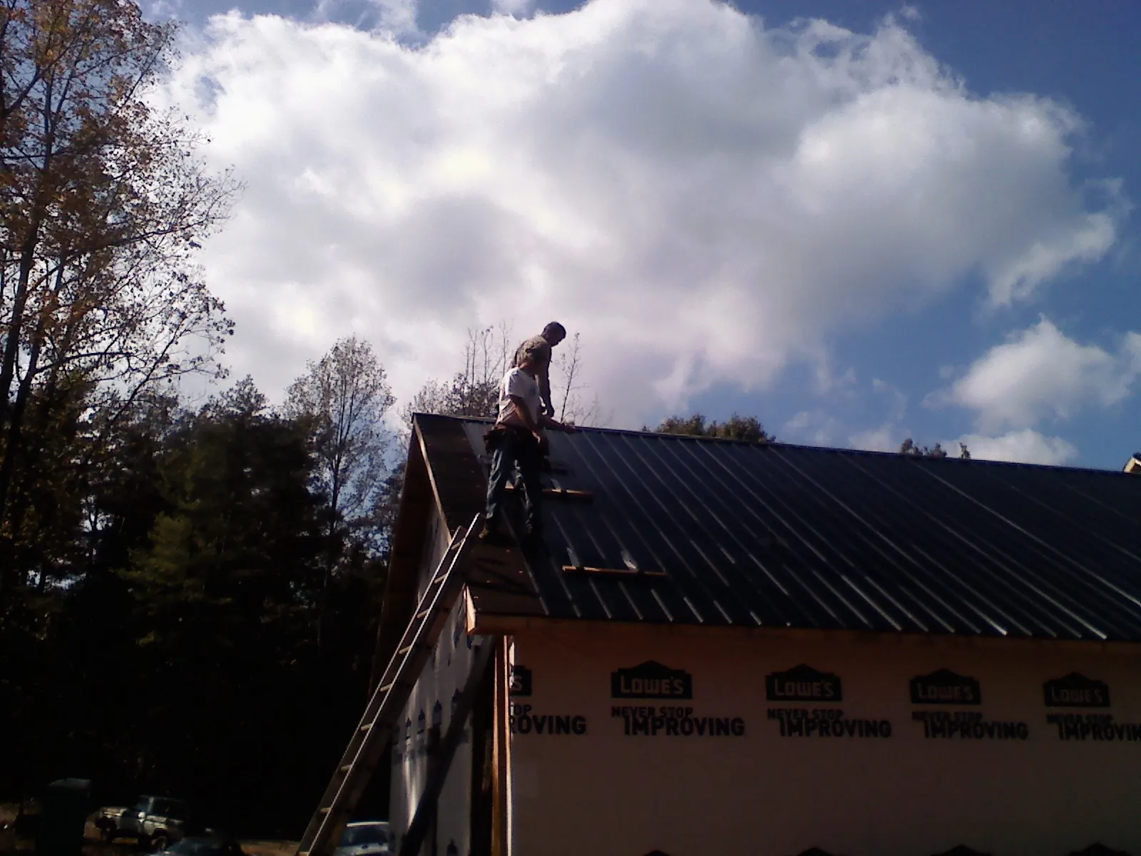 Roofer fastening dark metal panels high against a cloudy sky in Rushville